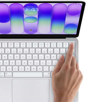 MacBook Neo color argento che mostra la schermata di login, con il dito di una persona appoggiato sul sensore Touch ID nell’angolo in alto a destra della tastiera
