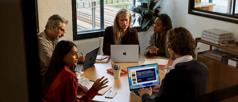 Un team di cinque persone sedute a un tavolo in una sala riunioni; per la riunione vengono utilizzati tre MacBook Pro.