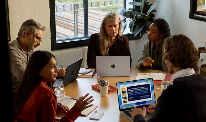 Un team di cinque persone sedute a un tavolo in una sala riunioni; per la riunione vengono utilizzati tre MacBook Pro.