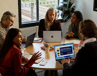 Un team di cinque persone sedute a un tavolo in una sala riunioni; per la riunione vengono utilizzati tre MacBook Pro.